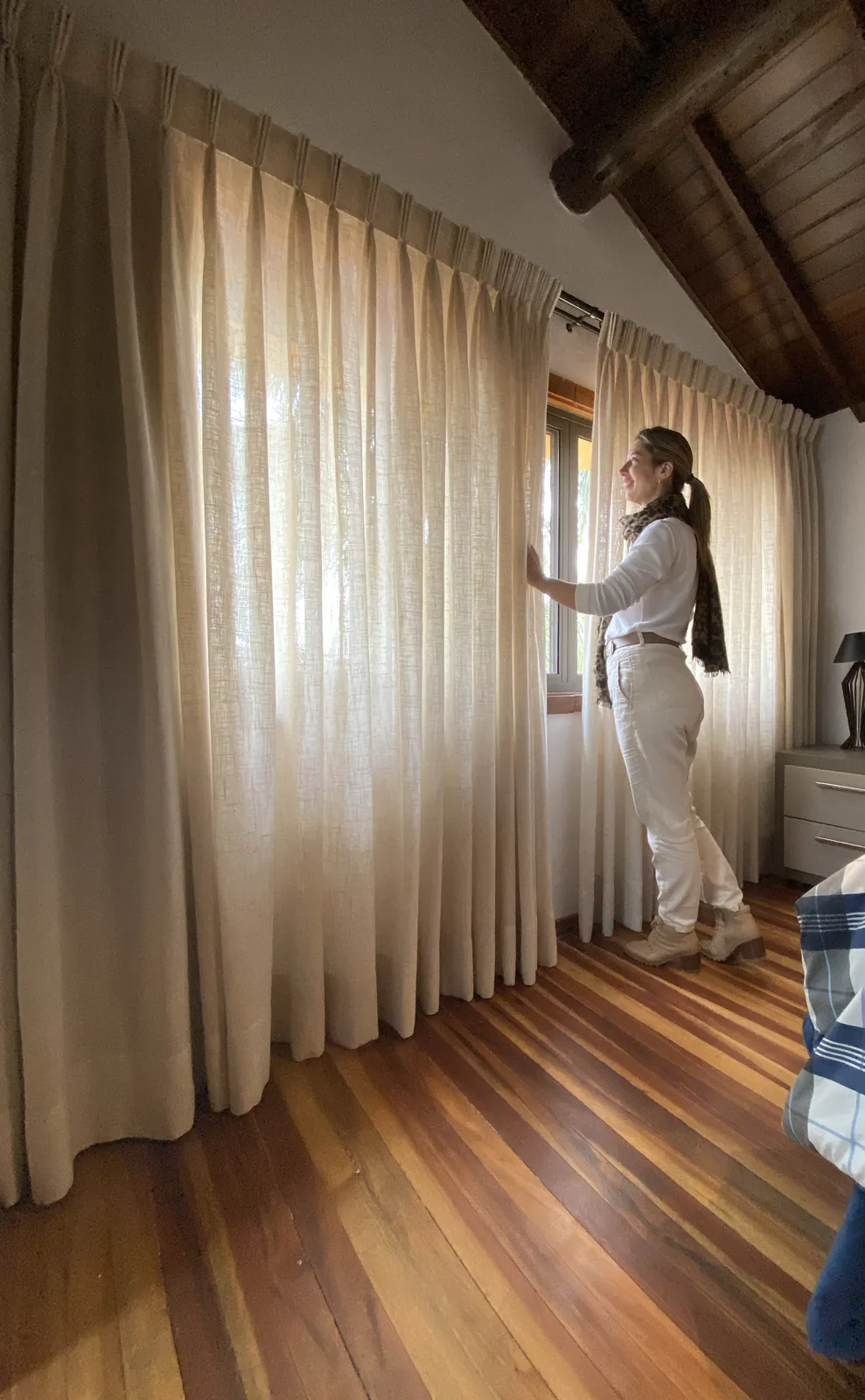 Lauren ajustando cortina de tecido clara em um quarto